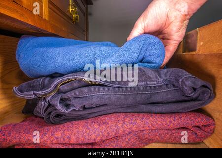 Nahaufnahme von der Hand eines Mannes, der gefaltete Gegenstände mit sauberer Kleidung in eine alte Holzschublade legt. Stockfoto