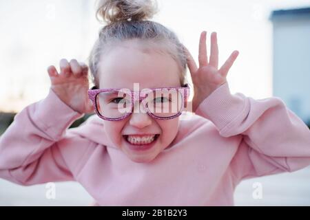 Porträt eines jungen Mädchens zieht lustige Gesichter mit rosa funkelnden Gläsern Stockfoto