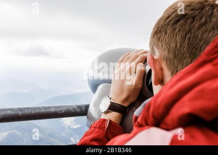 Der junge blonde Mann schaut aus der Beobachtung in Ferngläsern auf die Berge Stockfoto