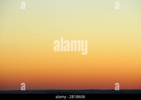 Flammender Himmel über dem Horizont bei Sonnenuntergang oder Sonnenaufgang. Leuchtend schillernde Farben von Gelb, Orange und Rot. Farbiger Hintergrund für Text und Design. Stockfoto