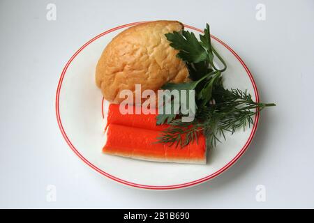 Stillleben von einem Stück Weißbrot, Krabbenstäbchen und Petersilie auf einer weißen Platte mit rotem Rand. Stock-Foto für Web und Print, Papierwalzer und Hintergrund. Stockfoto