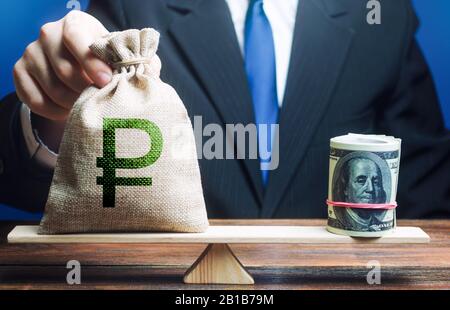 Man legt einen russischen Rubelgeldbeutel auf eine Waage, die dem Dollarbündel entgegensteht. Geldpolitik. Zentralbank-Regulierungsbehörde. Marktschwankungen. Wechselkurs, c Stockfoto