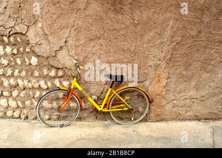 Farbenfrohes, gelb leuchtendes Fahrrad, das an der alten Lichtwand geparkt ist. Einsamer Einzelgänger allein ein verlassenes Fahrrad auf einer Straße. Stockfoto