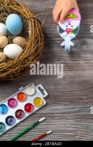 Ostereier im Gelege und bunte Farben und Pinsel auf Holzhintergrund. Baby beginnt zu malen. Nahaufnahme Stockfoto
