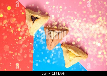 Purim Urlaubskonzept. Kreatives Arrangement von Vielfalt Hamantash auf rotem, pinkfarbenem und blauem hellem festlichem Hintergrund.Hamantaschen Dreiecksgebäck auch Haman's Taschen oder Oznei Haman-Haman's Ohren genannt. Stockfoto