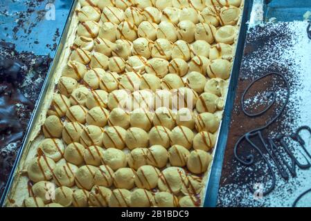 Köstlicher cremefaramelter Kuchen, mit Karamell auf das Schaufenster der Konditorei gestreut, daneben sieht man noch einen weiteren Schokoladenkuchen Stockfoto