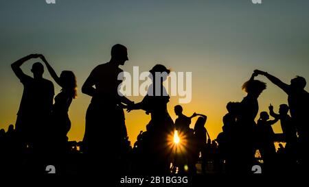 Romantische Silhouetten von Paaren, die bei Sonnenuntergang gegen den warmen Himmel tanzen Stockfoto