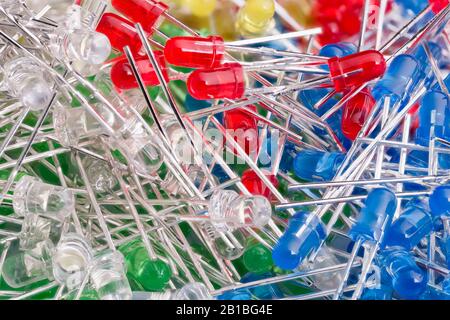 Kleine bunte LED-Dioden. Elektrotechnischer Hintergrund. Rote, blaue, grüne oder gelbe transparente Kunststoff-Elektronikkomponenten auf strukturierter Haufennaht. Stockfoto