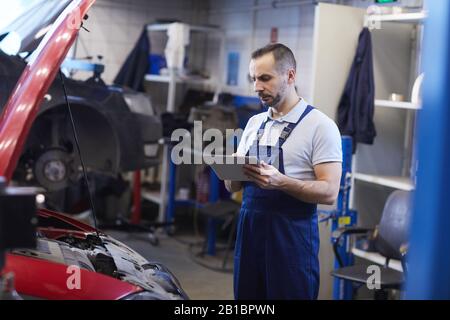 Portrait von bärtigen Automechanikern mit digitalem Tablett während der Fahrzeugkontrolle in der Werkstatt, Kopierraum Stockfoto