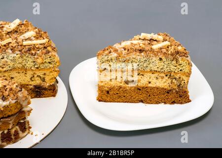 Schokoladenkuchen mit einem separaten Stück auf einer weißen Platte auf grauem Grund. Stockfoto