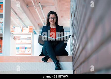 Eine Überlieferte Frau, Die ein Buch Liest Und Auf Stufen Sitzt Und Lächelt. Konzept Der Behinderten Person, Die Das Ganze Leben Lebt. Hochschulbildung Stockfoto