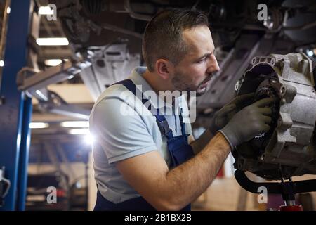 Seitenansicht Portrait von bärtigen Automechanikern Reparatur Getriebe in Auto-Werkstatt, Kopierraum Stockfoto