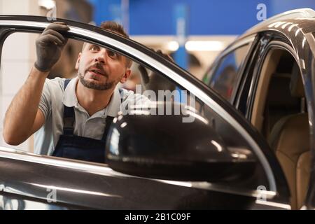Portrait von reifen Mechanikern, die die Isolierung an den Fenstern des Luxuswagens in der Werkstatt für die automatische Reparatur prüfen, Kopieraum Stockfoto