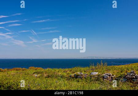 Malerischer Blick auf die Landschaft von Saltee Island über das Meer bis zur Küste von Wexford mit Windenergieanlagen in der Ferne. Windpark, der Strom erzeugt. Blauer Himmel Stockfoto