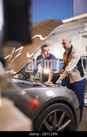 Durchgehender Portrait von zwei Automechanikern, die unter der Haube des Autos in der Werkstatt für automatische Reparaturen blicken, Kopieraum Stockfoto