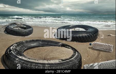 Autoreifen und Plastikflaschen verschmutzen in schlammiger Pfütze am Strand. (Umweltkonzept) Stockfoto