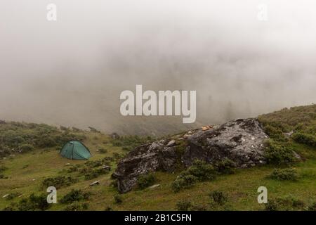 Ein einsames grünes Zelt steht im Nebel in den Bergen. Ein großer Felsbrocken im Vordergrund. Grüne Vegetation rund. Kopierbereich. Horizontal. Stockfoto
