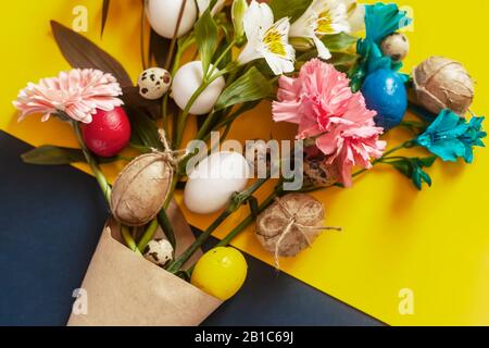 Ein wunderschöner Blumenstrauß mit bunten Frühlingsblumen und Ostereiern auf dem bunten Papierhintergrund. Draufsicht. Frohe Ostern, Frühling, festliches fest Stockfoto