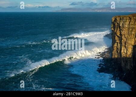 Große Wellen unter Klippen auf der westlichen Seite von Dunnet Head, Caithness, Schottland, Großbritannien. Die Insel Hoy, Orkney, in der Ferne. Stockfoto