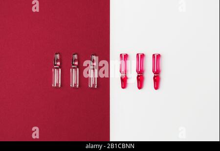Linie von Ampullen für Injektionszwecke mit roter und transparenter Flüssigkeit auf isoliertem weißem und dunkelrotem Hintergrund. Medizin-, Gesundheits- und Apothekenkonzept. F. Stockfoto