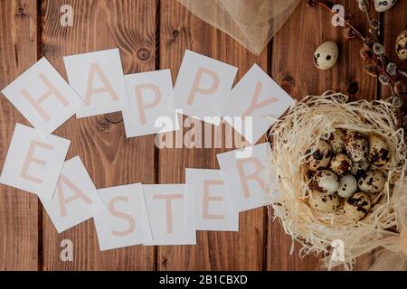 Flache Laienzusammensetzung aus Wachteleiern und Karte mit Text Happy Easter auf Holztisch. Draufsicht. Stockfoto