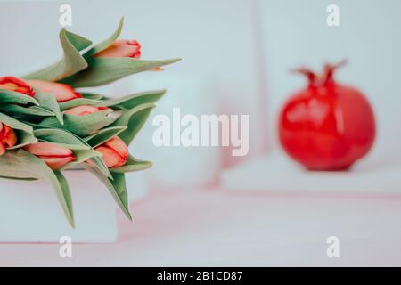 Frühlingsblumen rote Tulpen und keramische Granatapffrucht auf weißem rosafarbenem Grund. Kopierbereich, getont Stockfoto