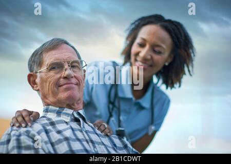 Porträt eines lächelnden Seniors, der von einer weiblichen Krankenschwester getröstet wird. Stockfoto