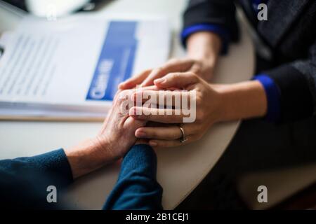 Hände von mittleren Erwachsenen und älteren Frauen halten sich gegenseitig auf einem Tisch. Stockfoto