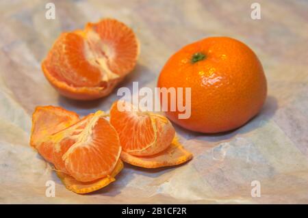 Eine Mandarine geschält und neben einer anderen mit Haut auf einem zerknitterten Wickelpapier geöffnet Stockfoto