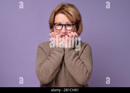 Ältere kaukasische Frau, die eine Brille trägt, die gestresst und nervös aussieht und die Hände an den Nägeln am Mund beißt. Angstproblem. Stockfoto