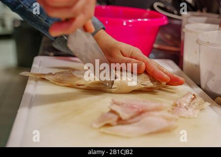 Küchenchef verwendet das Messer zum Schneiden und Schneiden von rotem Snapperfisch auf weißem Hackblock und in Scheiben geschnittenen Fischfilets auf der Arbeitsplatte in der Küche. Stockfoto