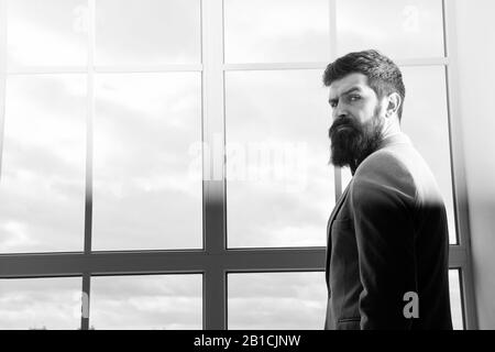 Das moderne Leben. business Mann am Fenster stehend mit Stadtbild. Brutale bärtiger Mann. Reifen Hipster mit Bart. Männliche im modernen Büro. Geschäftsmann in Anzug. Das moderne Leben des Geschäftsmannes. Stockfoto