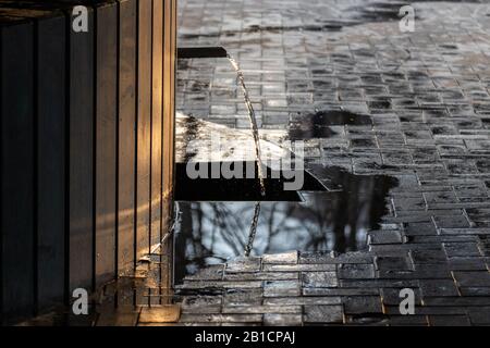 Klares Wasser aus der Trinkquelle funkelt bei Sonnenuntergang und läuft von einer dunklen Quelle aus schwarzem Stein. Natürliches Spülwasser. Stockfoto