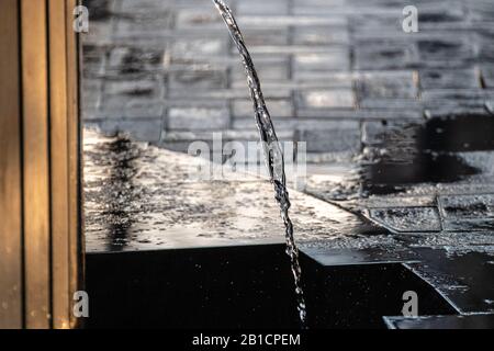 Klares Wasser aus der Trinkquelle funkelt bei Sonnenuntergang und läuft von einer dunklen Quelle aus schwarzem Stein. Natürliches Spülwasser. Stockfoto