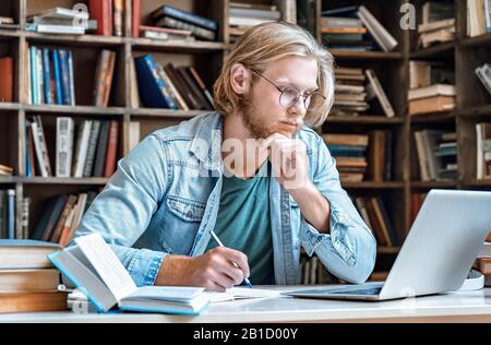 Der speziell auf junge Leute ausgerichtete Büchertisch, der moderne Laptop liest, macht sich Notizen und macht das Bildungskonzept Stockfoto