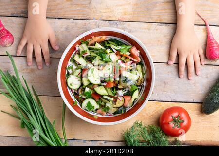 Kinder bereiten frischen gesunden Salat in der Nähe von verschiedenen Gemüse- und Obstsorten auf Holztisch vor, flacher Lay Stockfoto