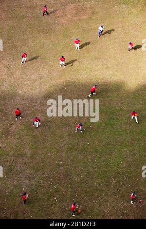 Eine Gruppe von Baseballspielern, die rotes Trikot tragen, übt ihre Kugelstoßkunst aus der Luftperspektive auf dem Feld aus. Stockfoto