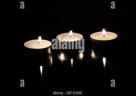 Drei brennende Teekerzen auf schwarzem Hintergrund, Nahaufnahme. Stockfoto