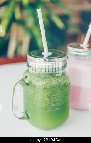 Gesunde Smoothie-Optionen in umweltfreundlichen Glasgefäßen mit Papierstraten in einem luxuriösen Fitnessbereich oder einem veganen Café. Trendige gedämpfte Tonbildung, Platz für Text Stockfoto