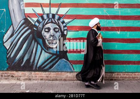 Muslimischer Kleriker spaziert vor anti-US-amerikanischem Wandbild mit Freiheitsstatue an den Wänden der ehemaligen US-Botschaft in Teheran Stockfoto