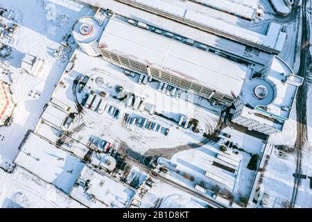 Schneebedecktes Industriegebiet mit Lagerhäusern, Fabrikgebäuden und geparkten Autos im Winter. Luftbild Stockfoto