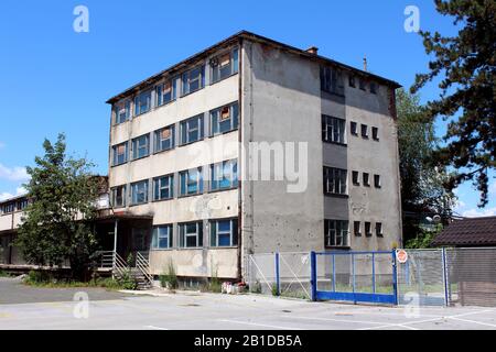 Verlassene kleine Bürogebäude mit gerissener baufälliger Fassade und teilweise mit gepflasterten Parkplätzen und Drahtzaun umgebenen Fenstern in alter Zeit Stockfoto