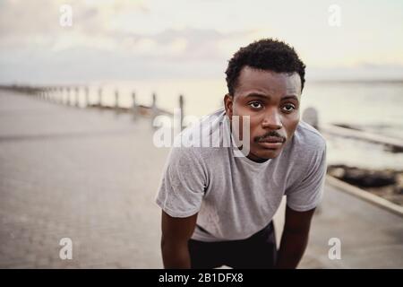 Junger sportlicher Mann in der Sportbekleidung sieht erschöpft aus und ruht sich morgens beim Joggen am Meer aus Stockfoto