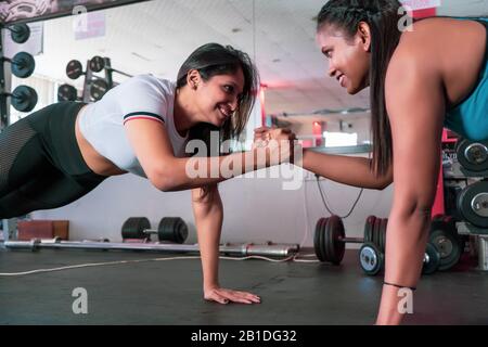 Zwei junge, motivierte, aggressiv attraktive, fokussierte, sportlich aktive Mädchen, die Push-Ups machen und die Hände zusammenhalten, während sie sich in der Moderne sehen Stockfoto