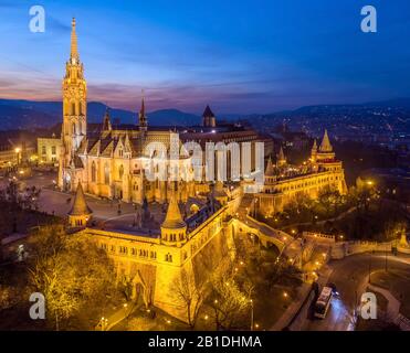 Budapest, Ungarn - Luftbild der beleuchteten Fischerbastei (Halaszbastya) und der Matthias Kirche in der Abenddämmerung mit Buda-Hügeln im Hintergrund Stockfoto