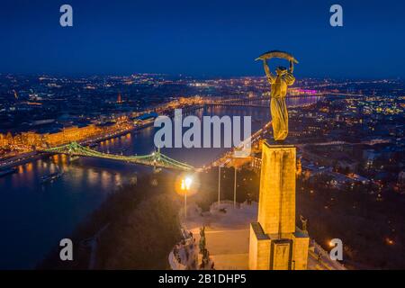 Budapest, Ungarn - Blick Auf Budapest mit beleuchteten Freiheitsstatue, Liberty-Brücke und Sightseeing-Booten auf der Donau zu blauer Stunde Stockfoto