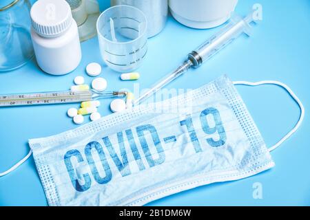 Eine Schutzmaske mit der Aufschrift COVID-19 neben medizinischen Instrumenten auf blauem Grund. Nahaufnahme. Stockfoto