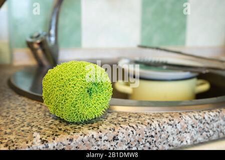 Grüner Kunststoff-Mesh-Geißel, zum Reinigen von Geschirr, Platten, Pfanne und Töpfen, in der Nähe des Spülkörpers in der Küche. Stockfoto