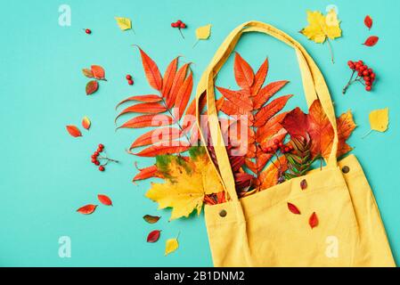 Herbst-Flachlaienzusammensetzung. Trockener Ahorn im Herbst in blauer Einkaufstasche auf gelbem Hintergrund. Draufsicht. Kopierbereich. Flaches Lay Stockfoto