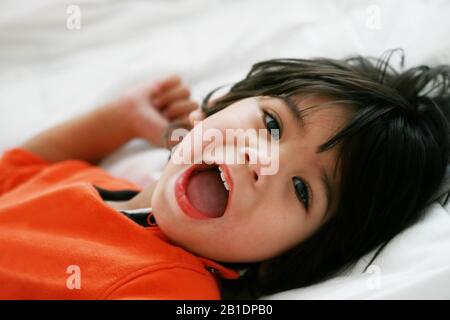 Hübsche kleine behinderte Junge, die orangefarbenes Hemd mit einem Lächeln auf der Kamera tragen Stockfoto